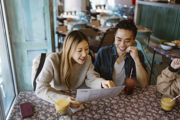 Smiling male and female friends reading menu while sitting together at restaurant