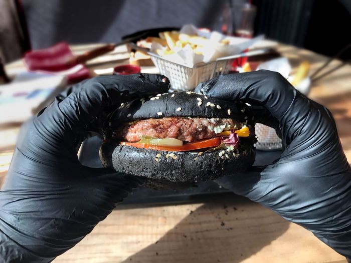 Close-up of hands in latex gloves holding black burger 
