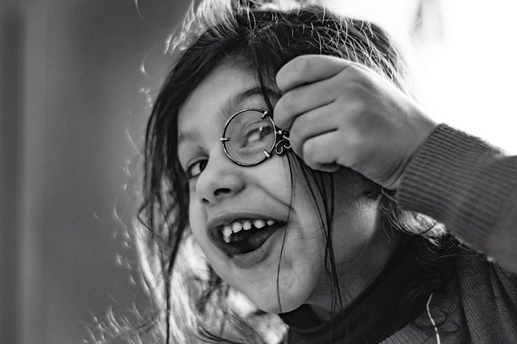 Close-up portrait of happy girl holding magnifying glass at home
