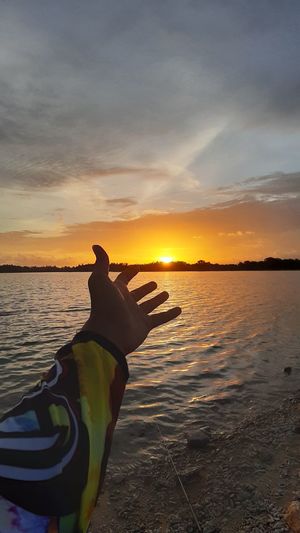 Woman hand by sea against sky during sunset