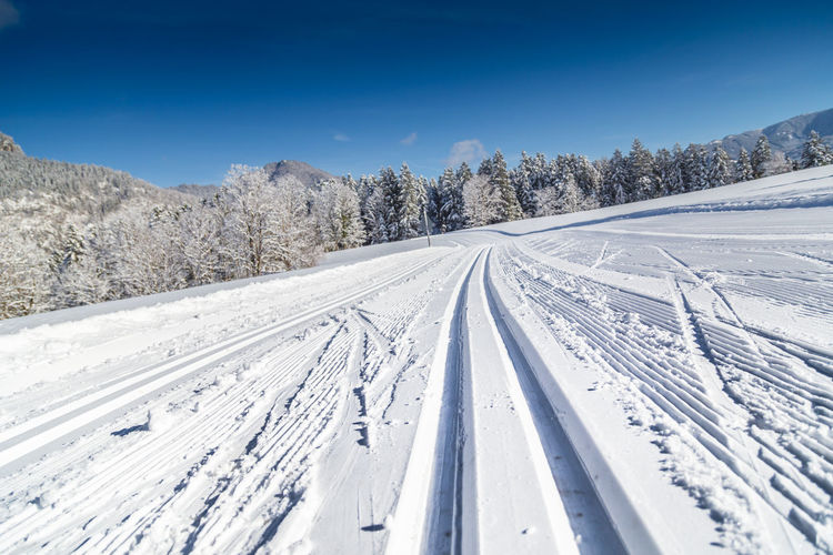 Tire tracks on snow covered land against blue sky