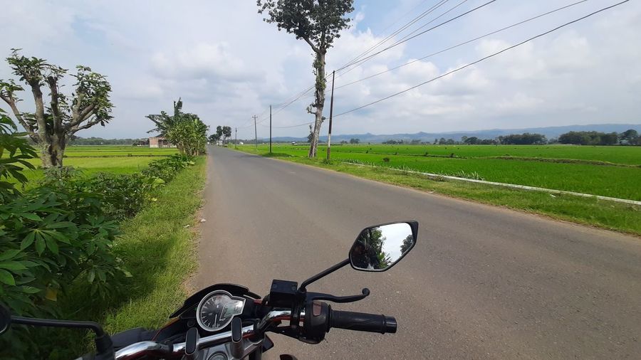 Motorcycle on road amidst field against sky