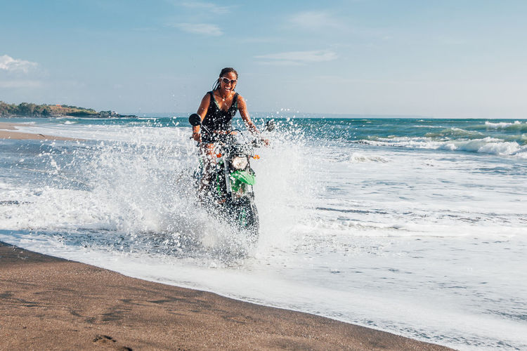Young woman splashing water while riding motorcycle at beach