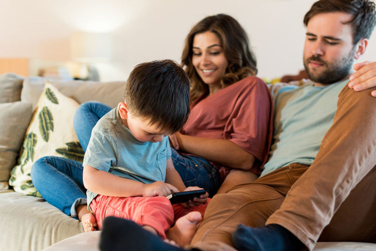 Parents looking at son using smart phone while sitting on sofa at home