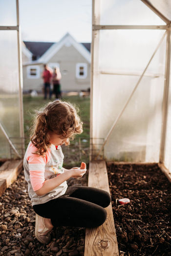Young girl sitting in backyard greenhouse and looking at seeds in hand