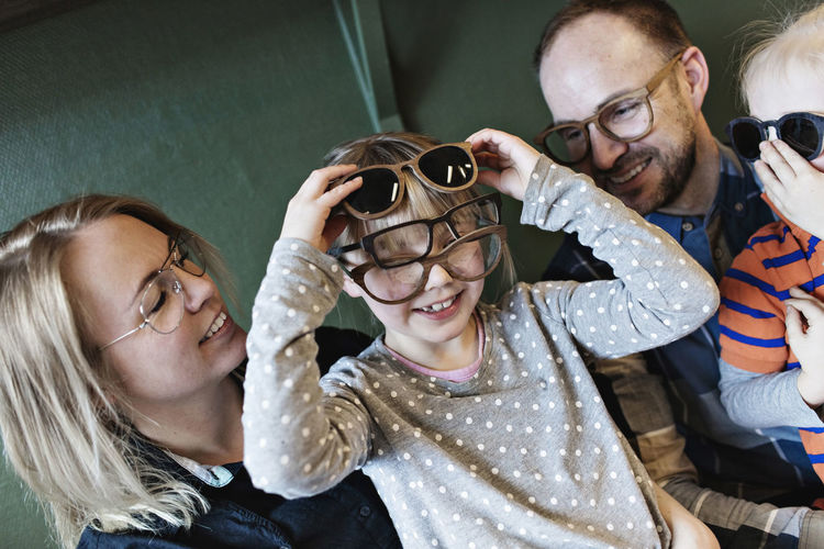 Happy family looking at girl wearing various eyeglasses on face at workshop