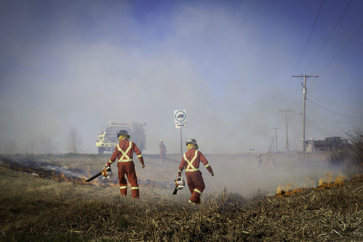 Rear view of firefighters standing on field against sky