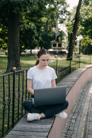 Young woman using digital tablet while sitting on bench in park