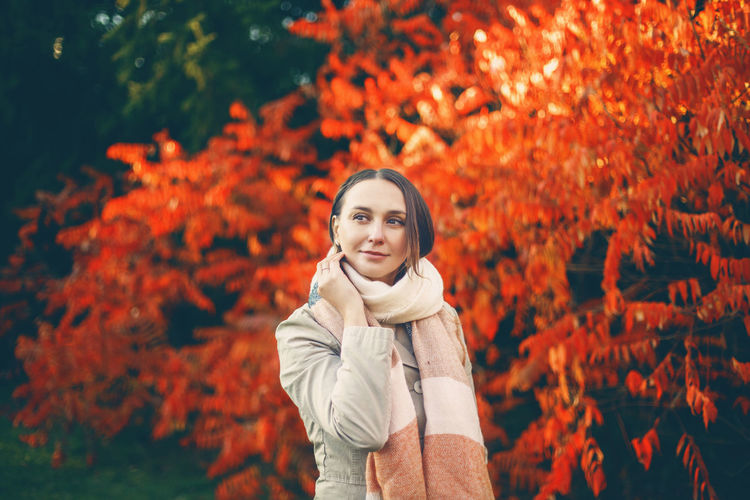 Portrait of young woman standing against orange tree during autumn