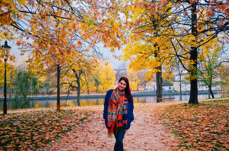 Portrait of young woman standing by leaves during autumn