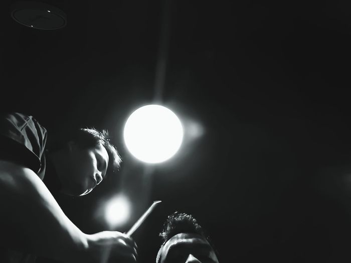 Low angle view of man hairstyling customer in darkroom