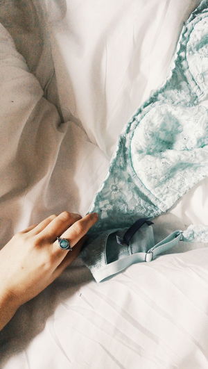 Cropped hand of woman holding lingerie on bed at home