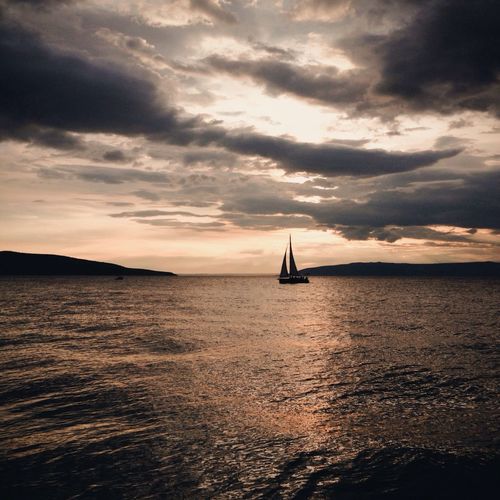 Boat sailing in sea against cloudy sky