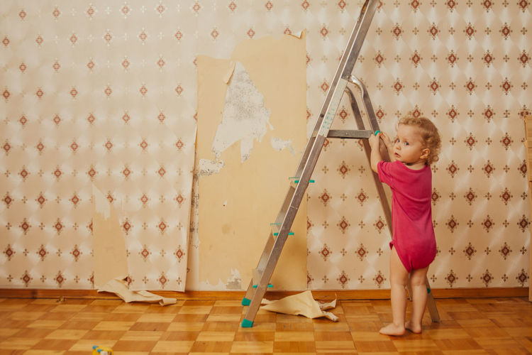 Child tear off the wallpaper from the wall in the room, little mother's helper