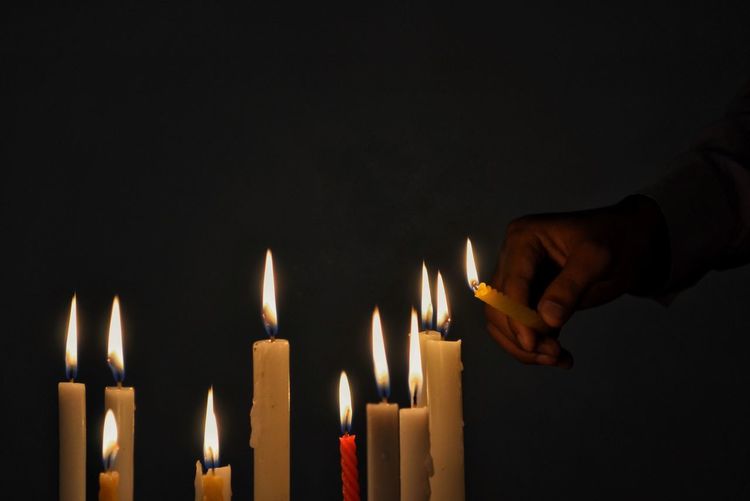Cropped hand igniting candles in darkroom