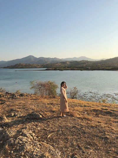 Full length of woman standing by lake against sky