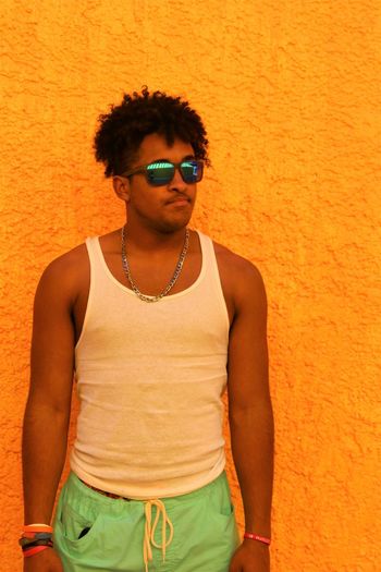Portrait of young man wearing sunglasses standing against orange wall