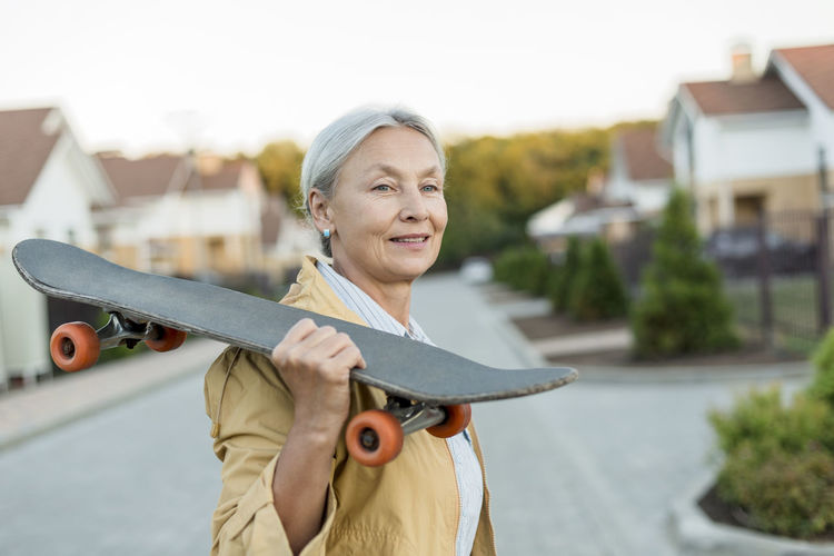 Portrait of smiling senior woman with skateboard on her shoulder