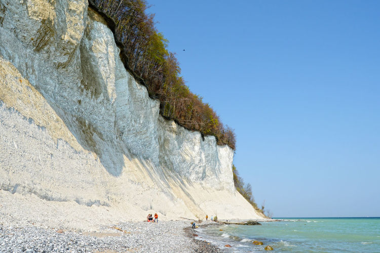 Low angle view of chalk cliff by sea against clear blue sky