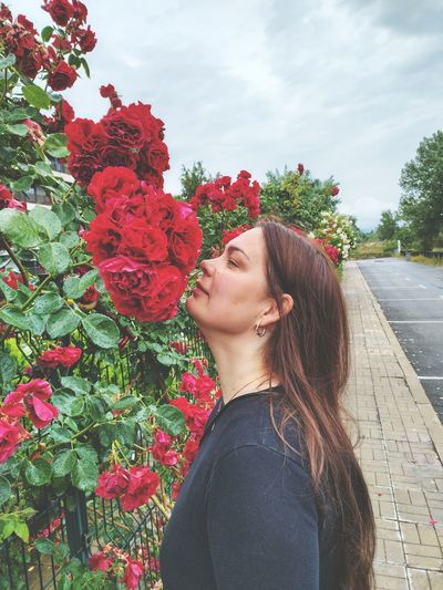 Portrait of young woman standing by flowering plants against sky