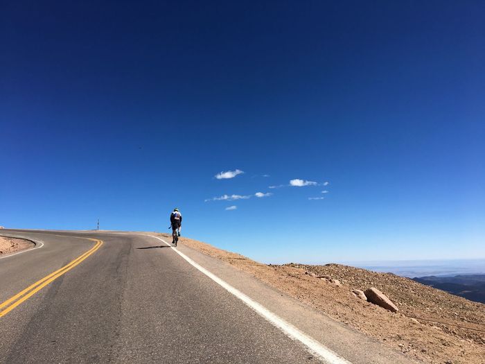 Rear view of man riding bicycle on road against clear blue sky