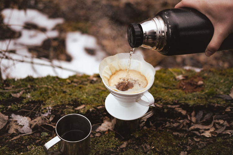 Brewing pour over coffee in nature at a hiking trip. hand pouring hot steaming water into a filter