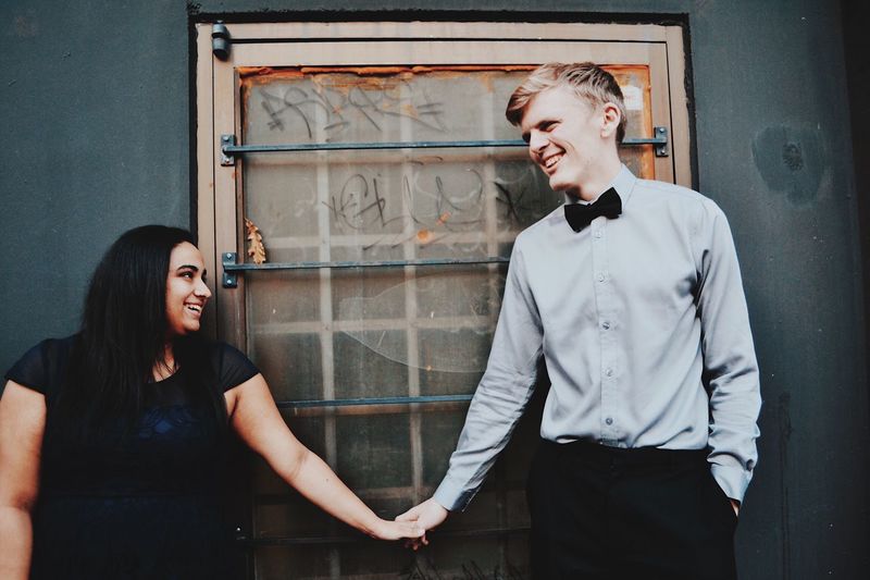 Smiling young couple holding hands while standing against wall