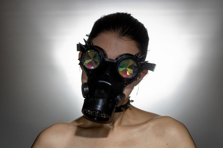 Shirtless young woman with gas mask against white background