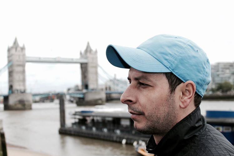 Close-up of thoughtful young man looking away with tower bridge over river thames in background