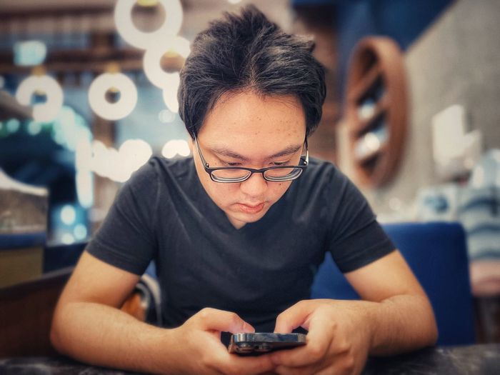 Young asian man using smartphone at table against circular led ceiling lights.