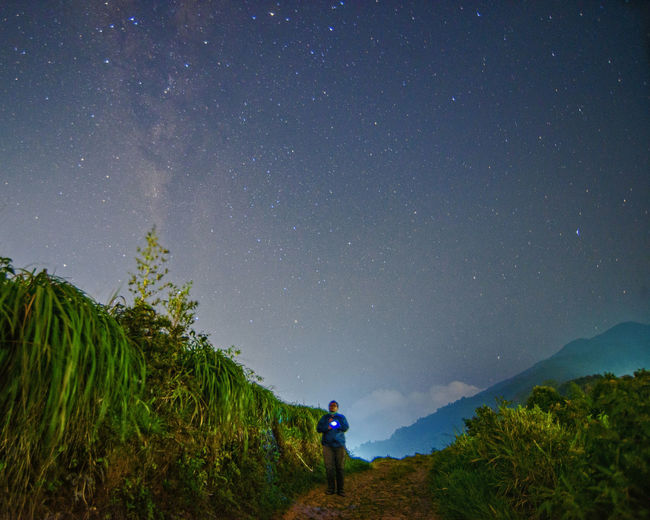 Rear view of man standing on field against sky at night