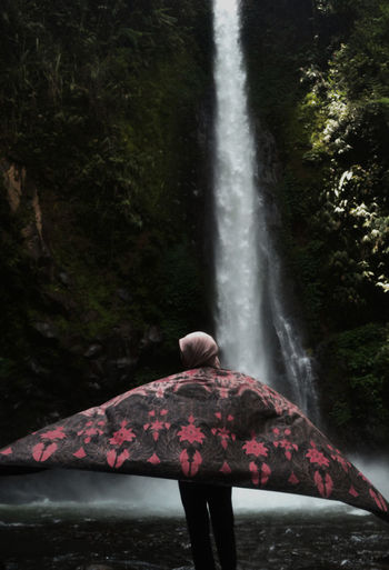 Rear view of woman with textile against waterfall