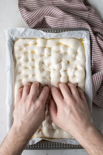 Top view of faceless person preparing raw dough for bread placed on baking paper on table