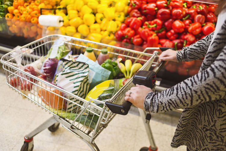 Midsection of woman pushing groceries in shopping cart at supermarket