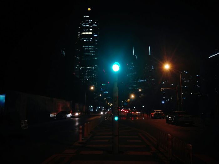 Illuminated road by buildings in city at night