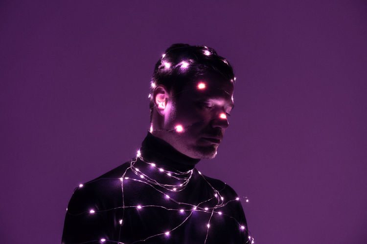 Man with illuminated string light against purple background