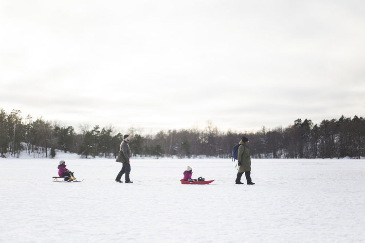 Parents pulling daughters on toboggan and sled during winter
