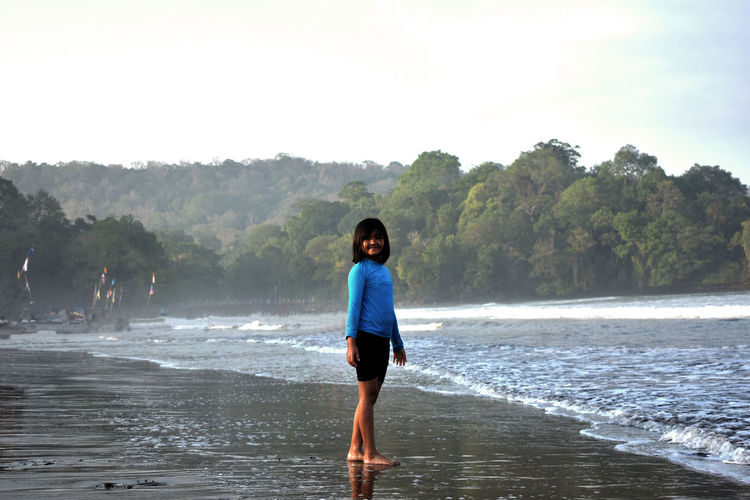 Full length of a young girl standing on beach against sky