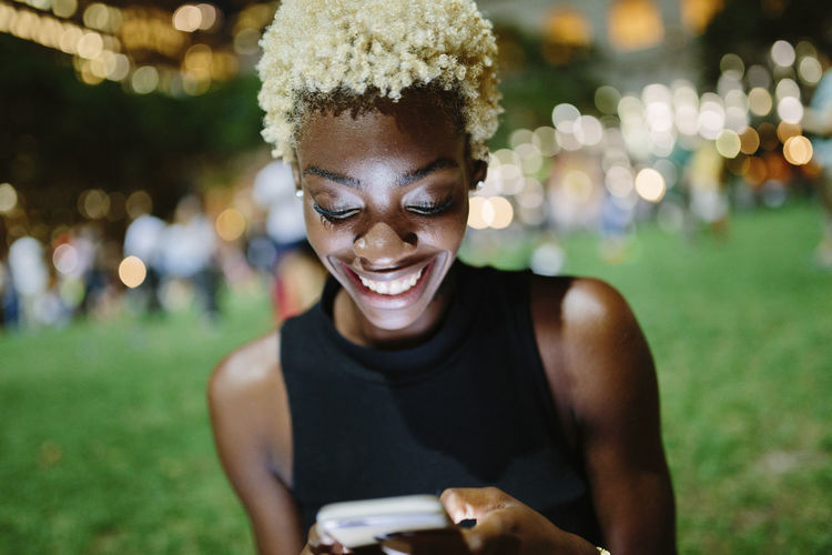 Young woman sitting in a park at night looking at cell phone