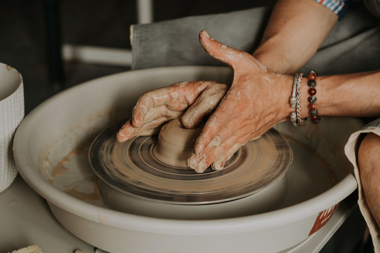 Close-up shot of ceramic cup spinning on potters's wheel and hands molding clay