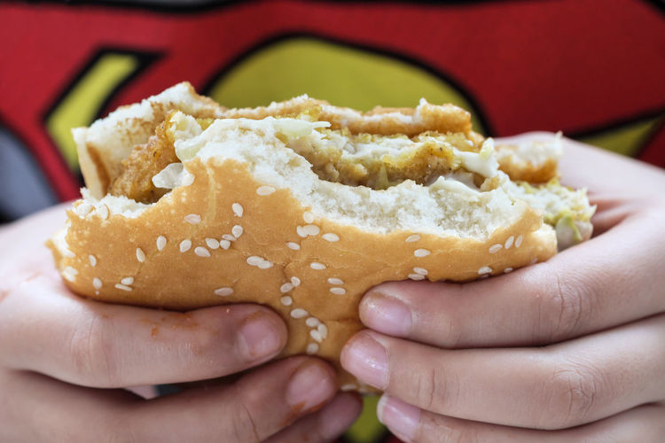 Close-up of hands holding half-eaten chicken burger. shallow depth of field.