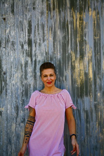 Portrait of smiling mature woman standing against wooden wall