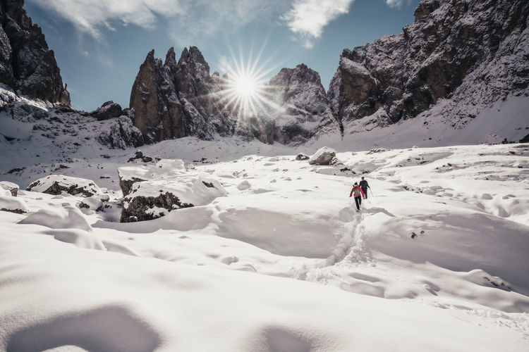 Two alpinists descending on snowy trail against sun rays in dolomites