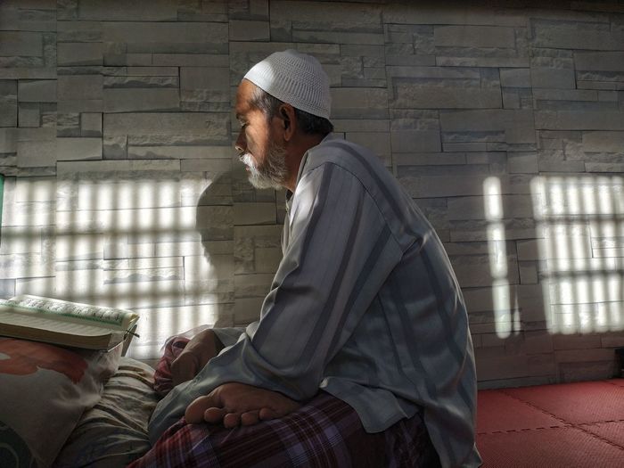 Side view of senior man reading koran at home