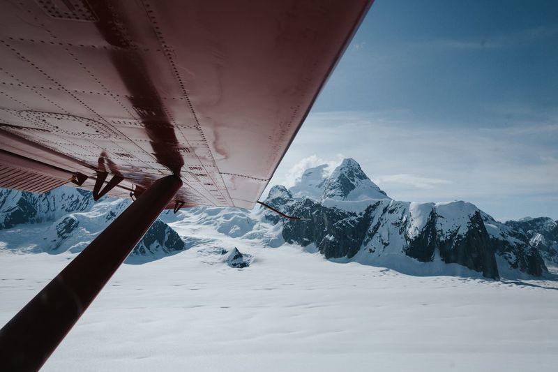 Cropped image of aircraft wing over snow covered land against sky