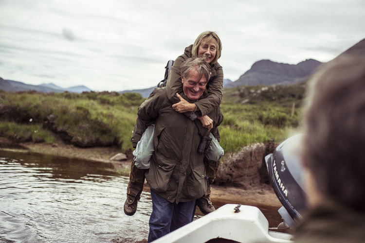 Retired couple piggy back carry across remote mountain fishing river