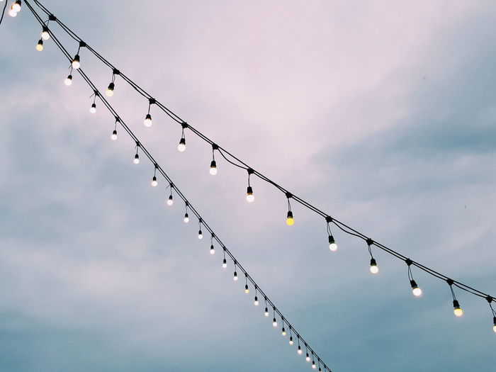 Low angle view of light bulbs hanging against sky