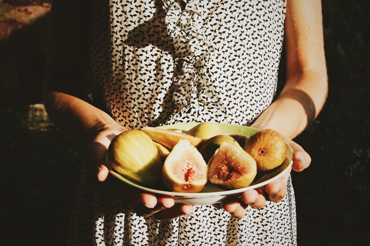 Midsection of woman holding figs on plate during sunny day