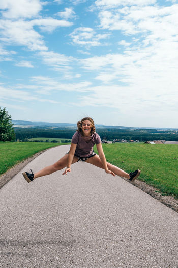 Portrait of smiling young woman jumping over road against sky