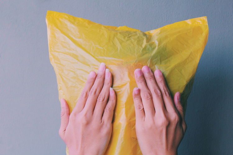 Close-up of woman wearing yellow plastic bag on face by wall